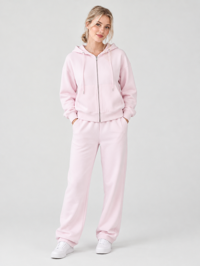 Woman wearing a light pink zip up hoodie and joggers tracksuit set, front view